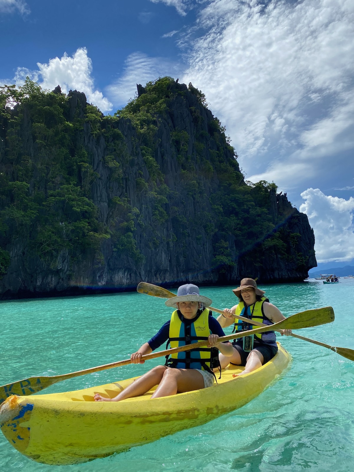 Two women in a kayak with an island cliffside in the background.