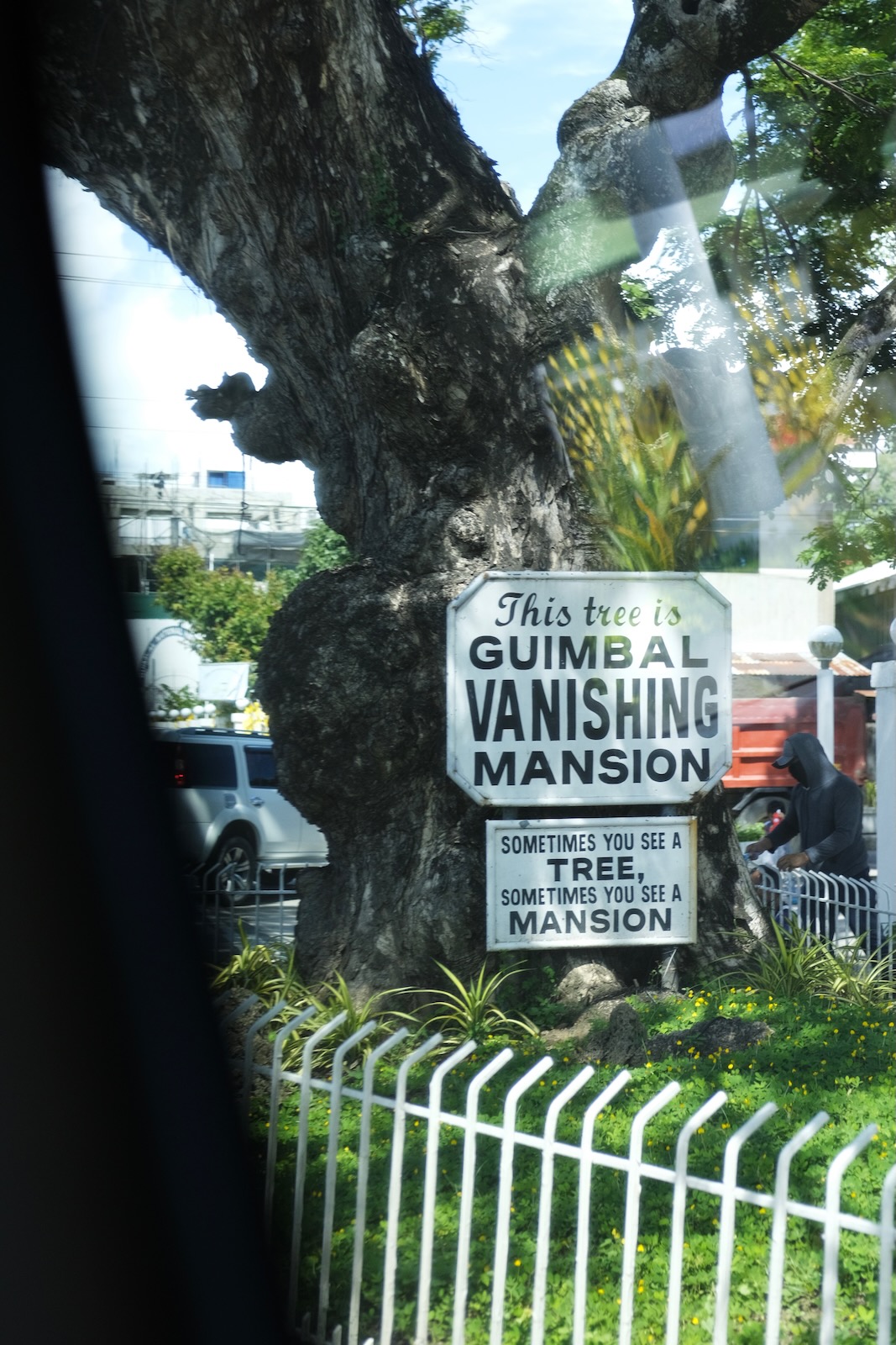 A sign in front of a large tree, marking the spot of Guimbal Vanishing Mansion.