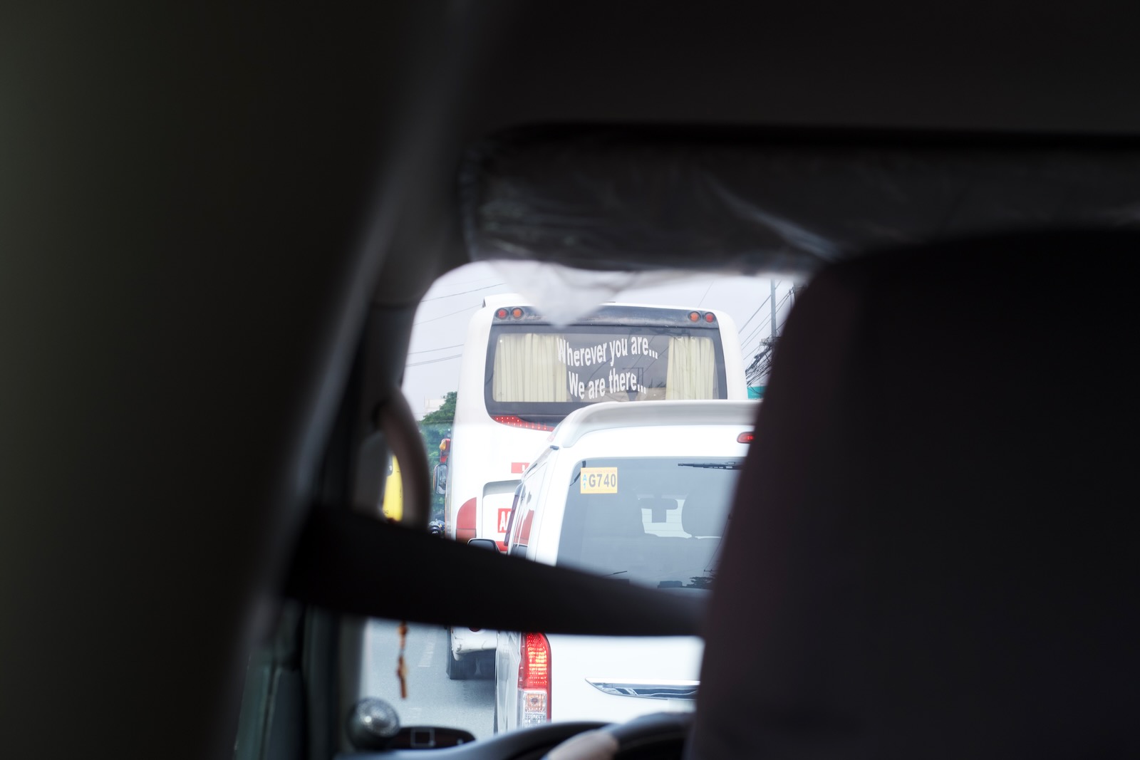 A view of traffic, shot from within a van. Through the windshield a bus is in view, with wavy text stenciled on the rear windshield saying “Wherever you are…We are there…”
