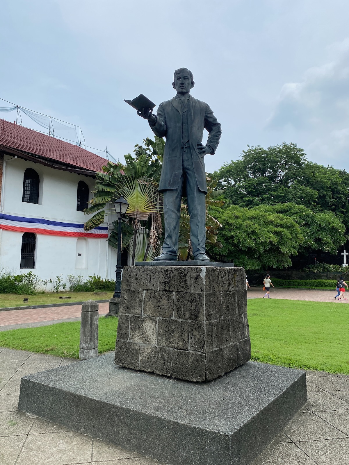 A metal statue of Jose Rizal atop a pedestal, looking out on a large courtyard.