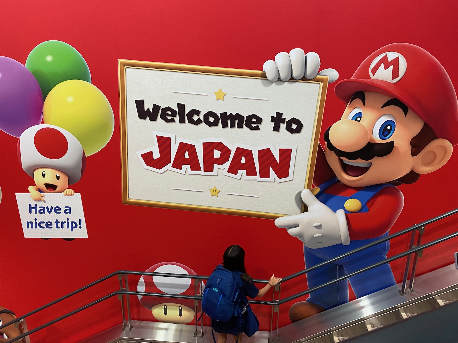Characters from Nintendo’s Super Mario video game series hold up signs welcoming travelers to Japan.