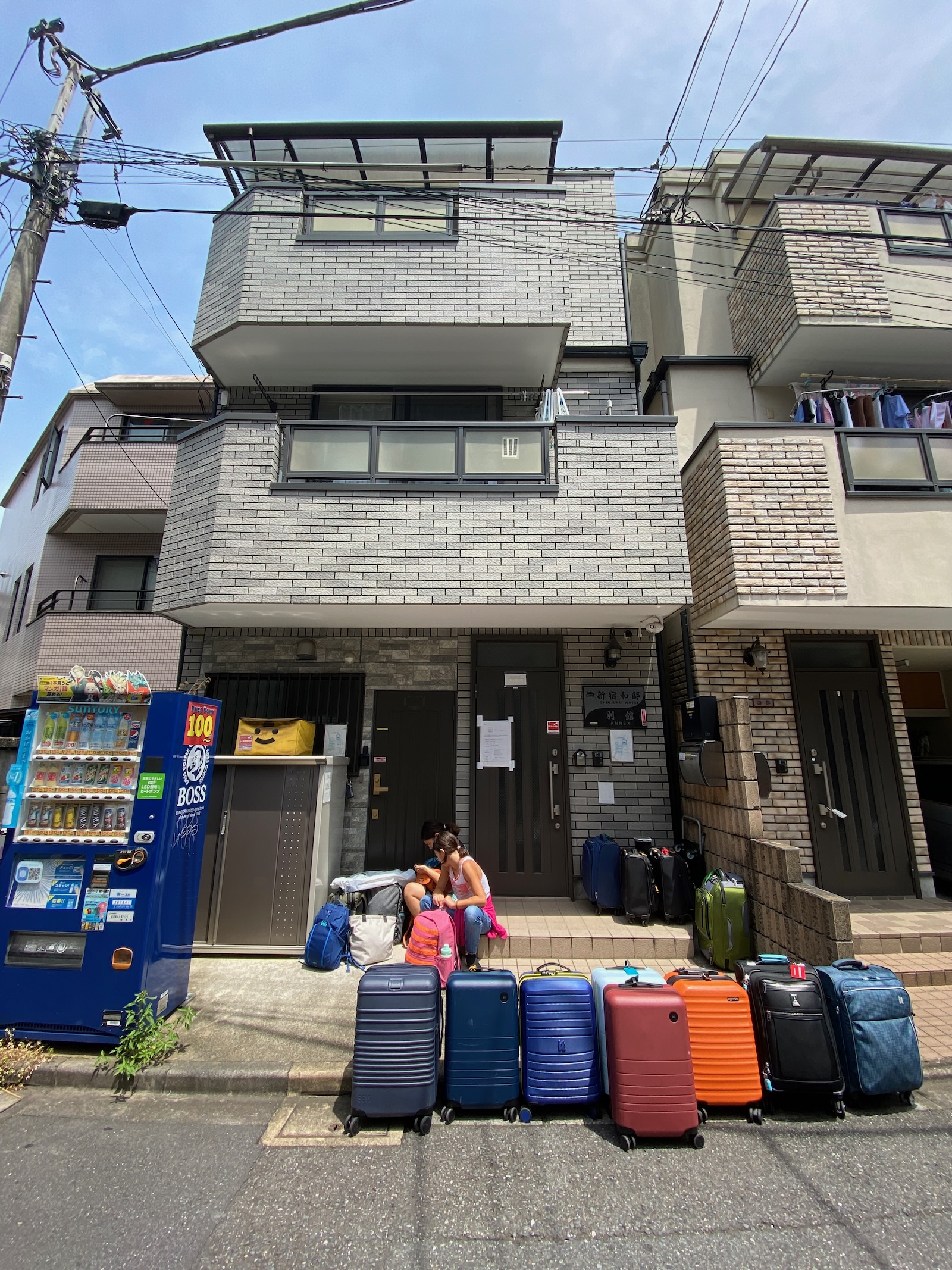 A row of colorful hard-sided rolling suitcases lined up outside an apartment building.