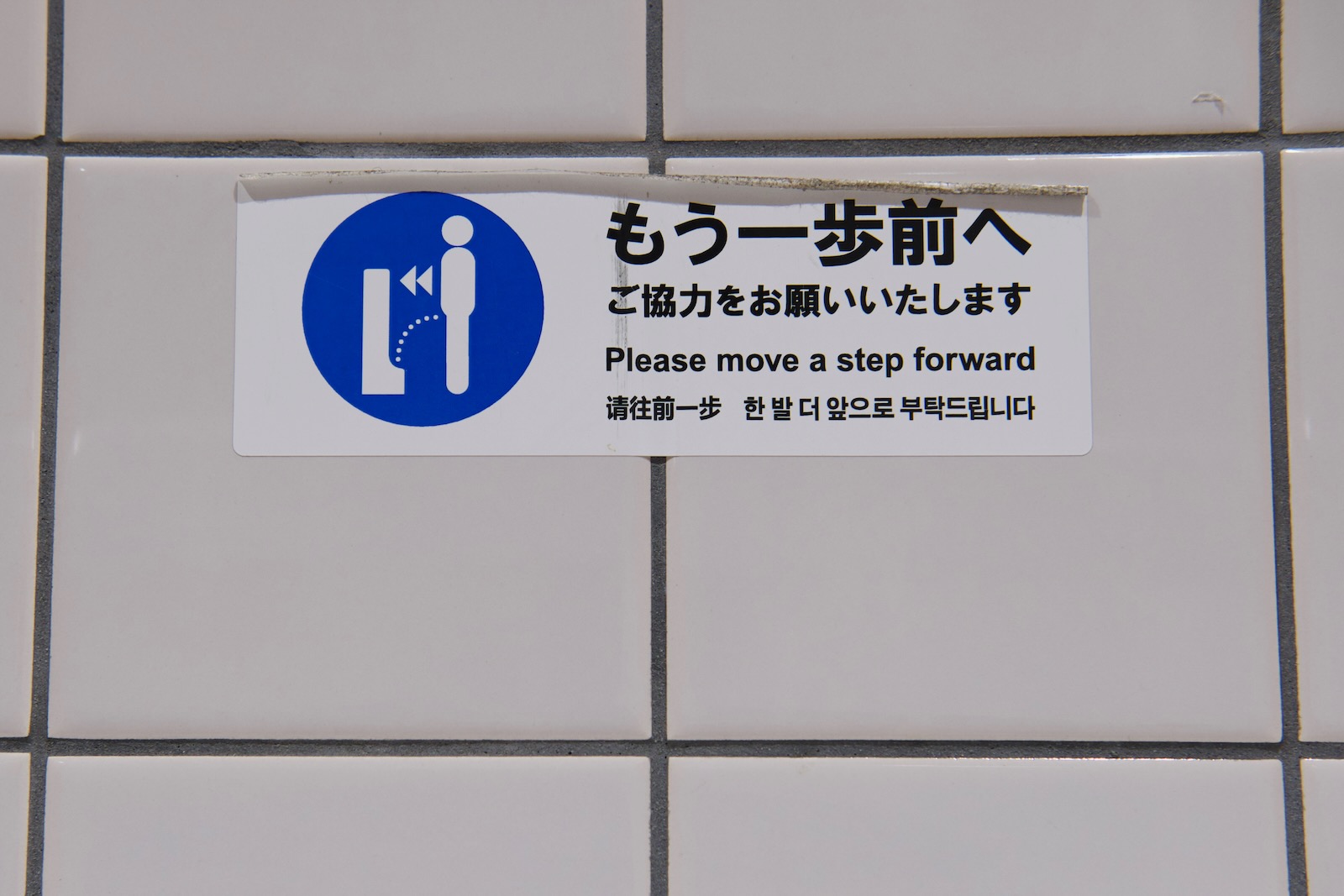Signage in front of a urinal urging people to step closer.