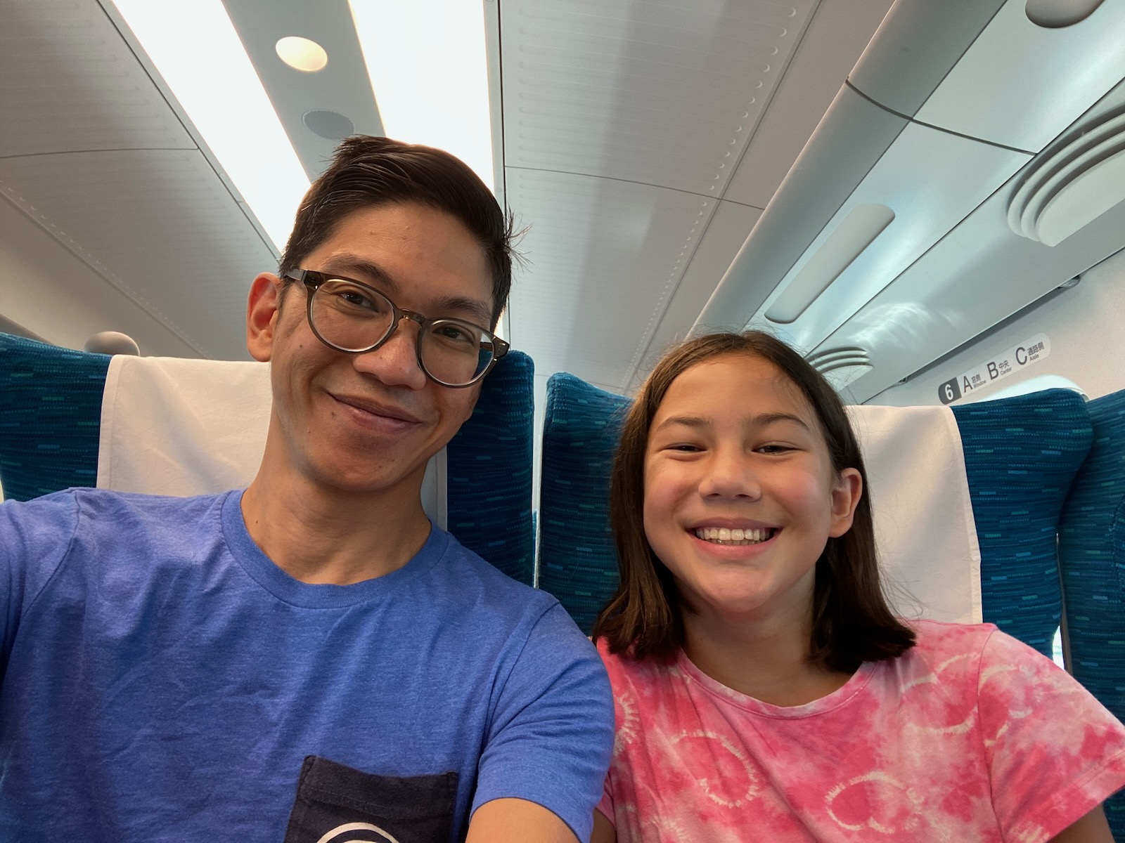 A man and his daughter sitting inside a Shinkansen rail car.