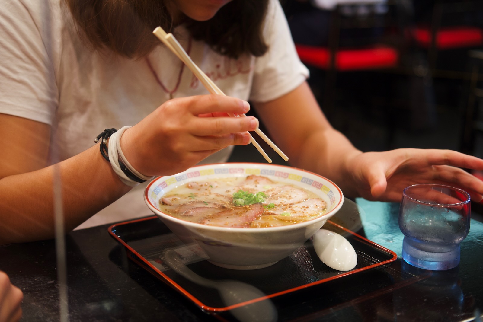 A girl holds chopsticks poised over a bowl of ramen.